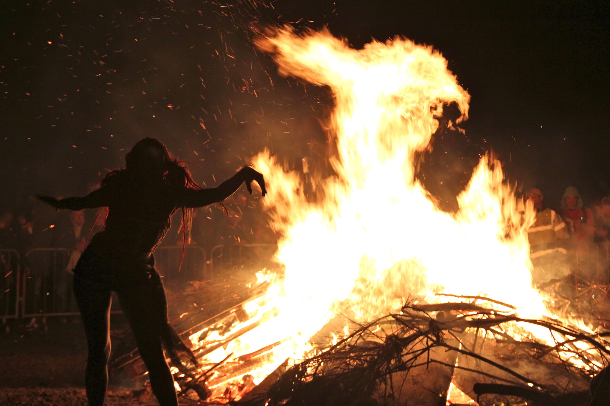 A partially naked woman seen only in dark shadow dances before a blazing bonfire.