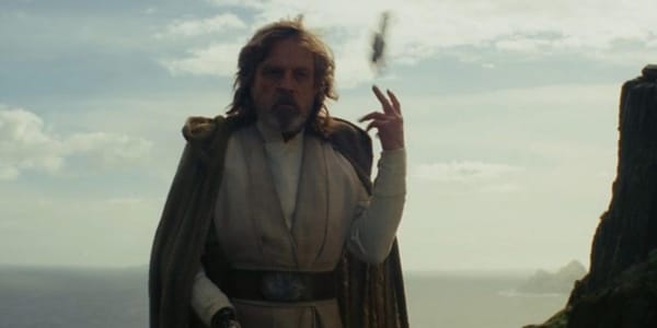 A wide shot of Luke Skywalker standing on a grassy cliff, tossing a legacy lightsaber over his shoulder.